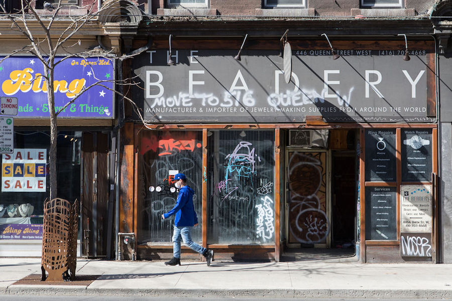 A person in a mask walks by a closed storefront with graffiti on it in Toronto on April 5, 2021