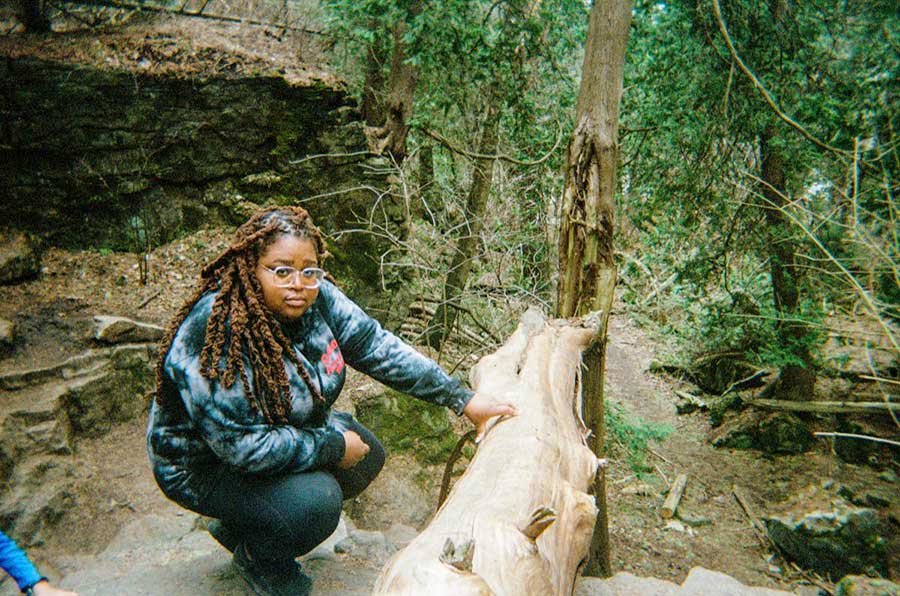 A photo of Kelly Fyffe-Marshall in the woods by a log