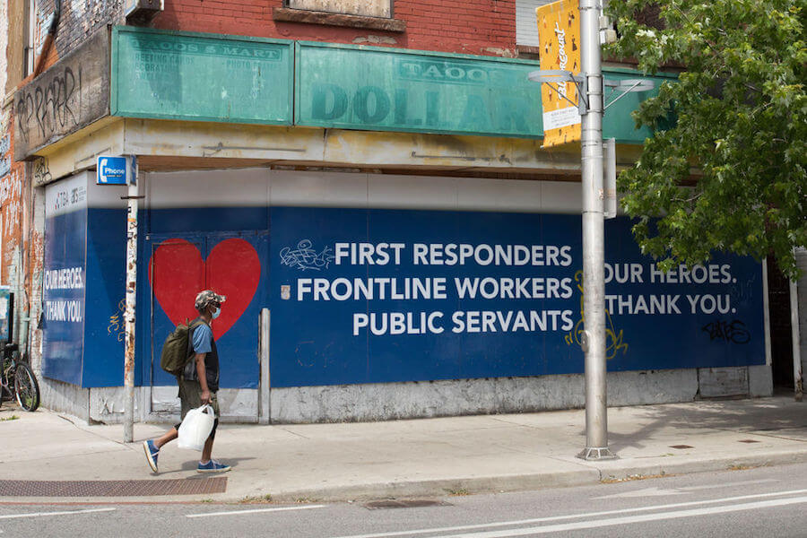 A person in a mask walks by a sign supporting first responders in Toronto