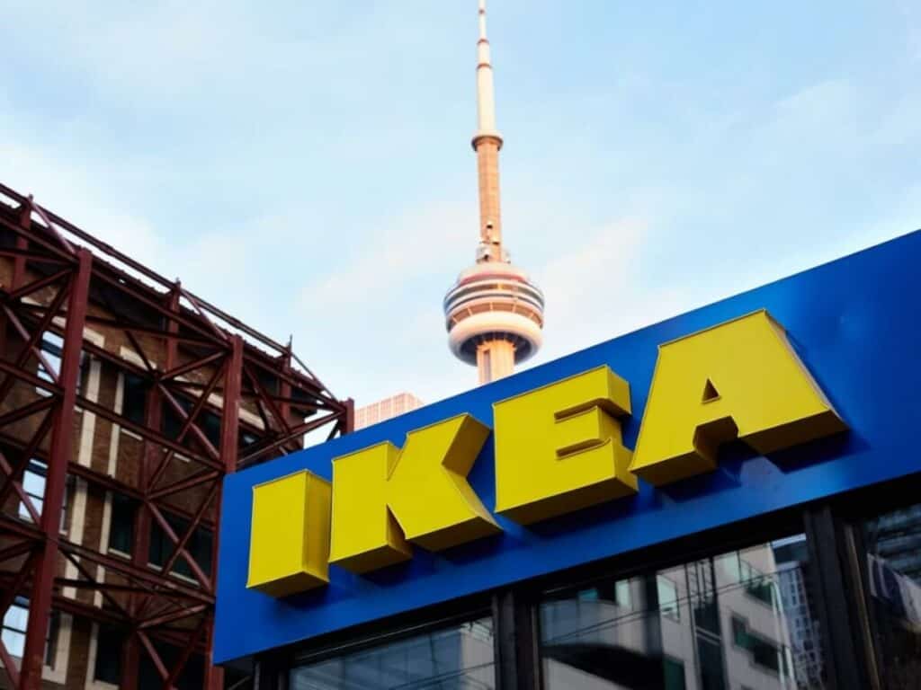 Bright yellow IKEA sign on a storefront with the CN Tower visible in the background in Toronto, Canada.