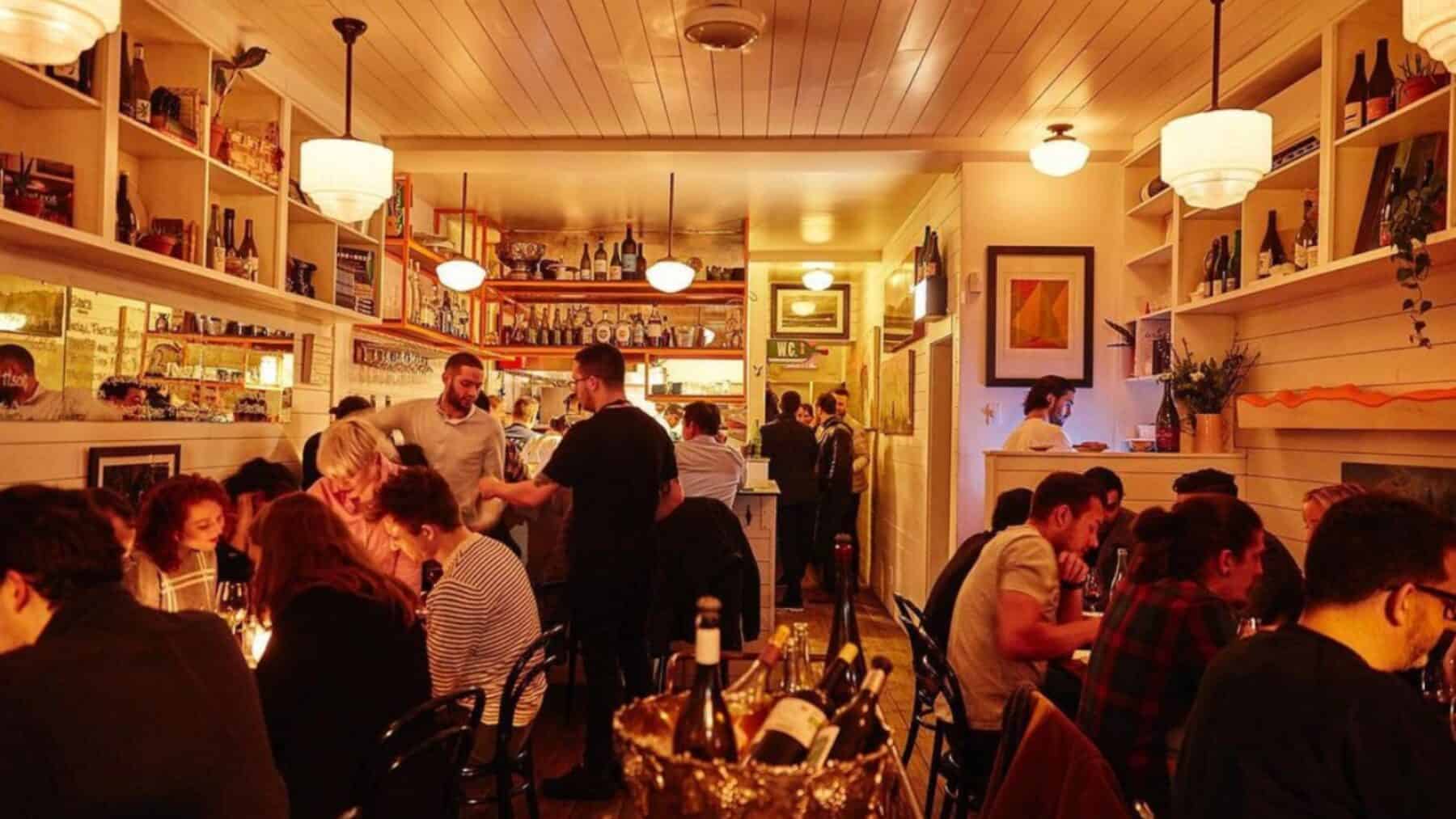 Cozy restaurant interior in Toronto with warm lighting, wooden decor, and a lively dining atmosphere, featuring guests enjoying their meals and wine.