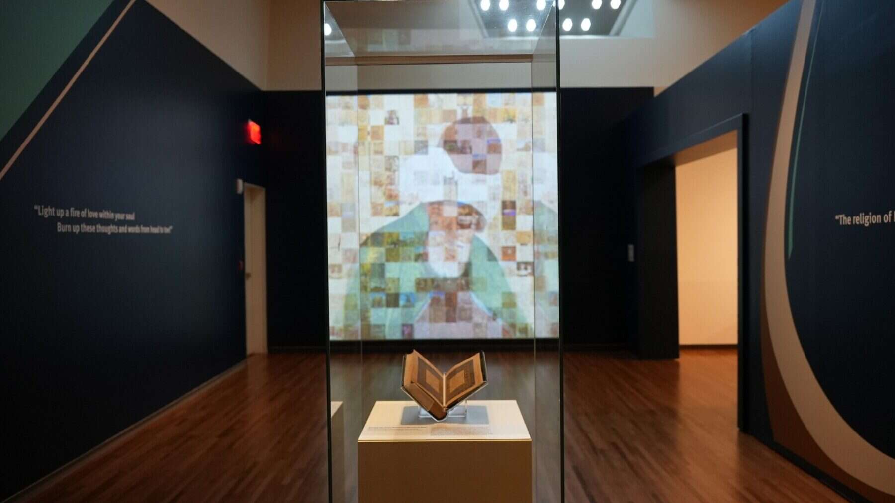 Vivid art exhibit featuring a digital mosaic portrait, illuminated display with an open book artifact, in a sleek modern gallery space.