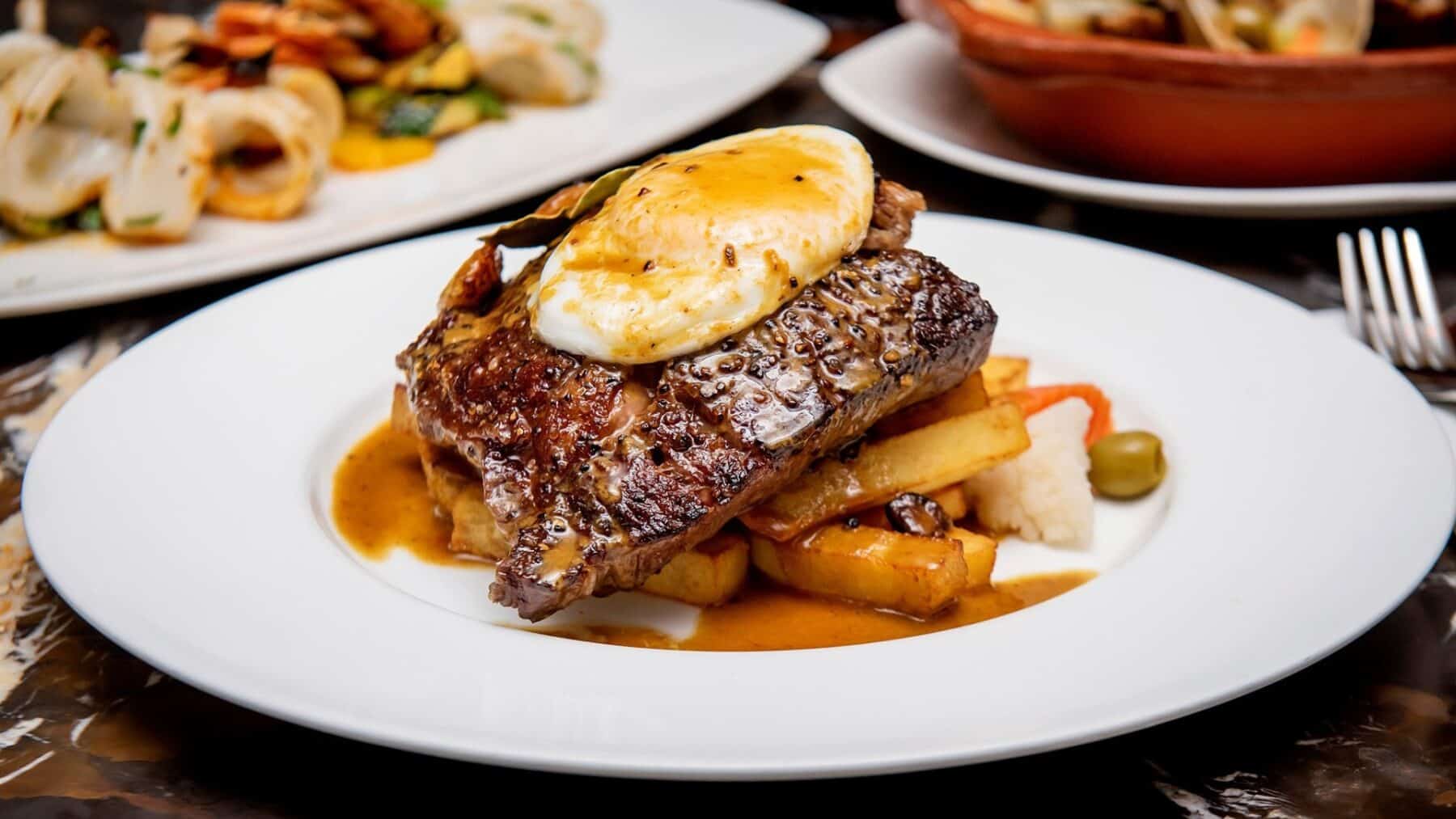 Juicy steak with a poached egg, roasted vegetables, and gravy on a white plate at a Toronto restaurant.