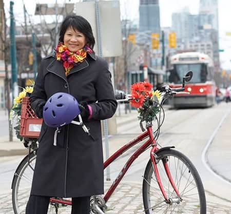 A woman with a bicycle on a city street, holding a helmet and smiling, showcasing Toronto cycling culture and outdoor activities in the city.