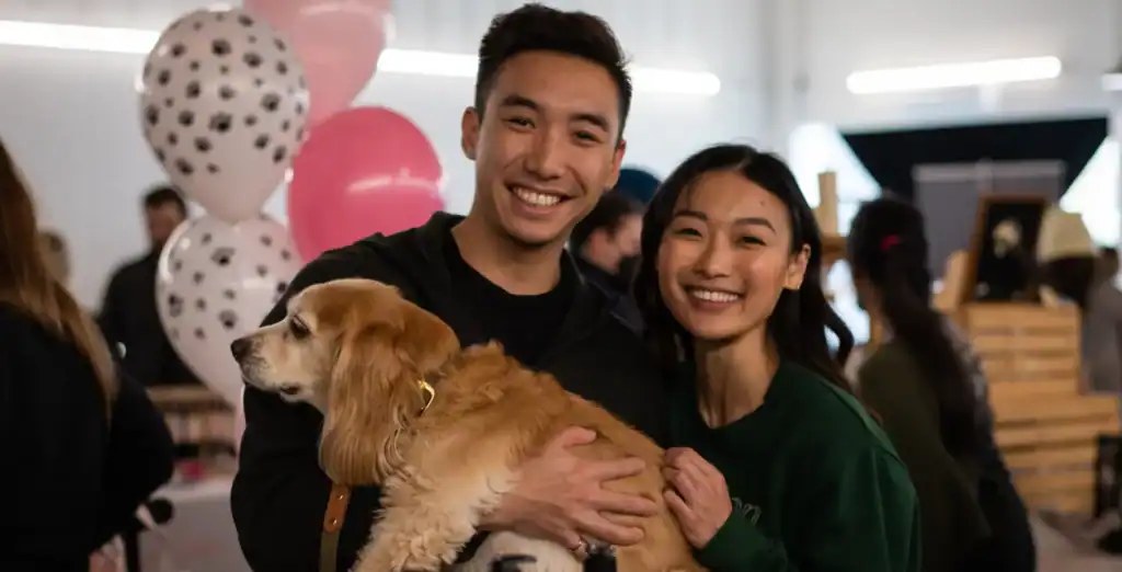 Happy young couple holding a friendly retriever dog at a lively indoor social event in Toronto.