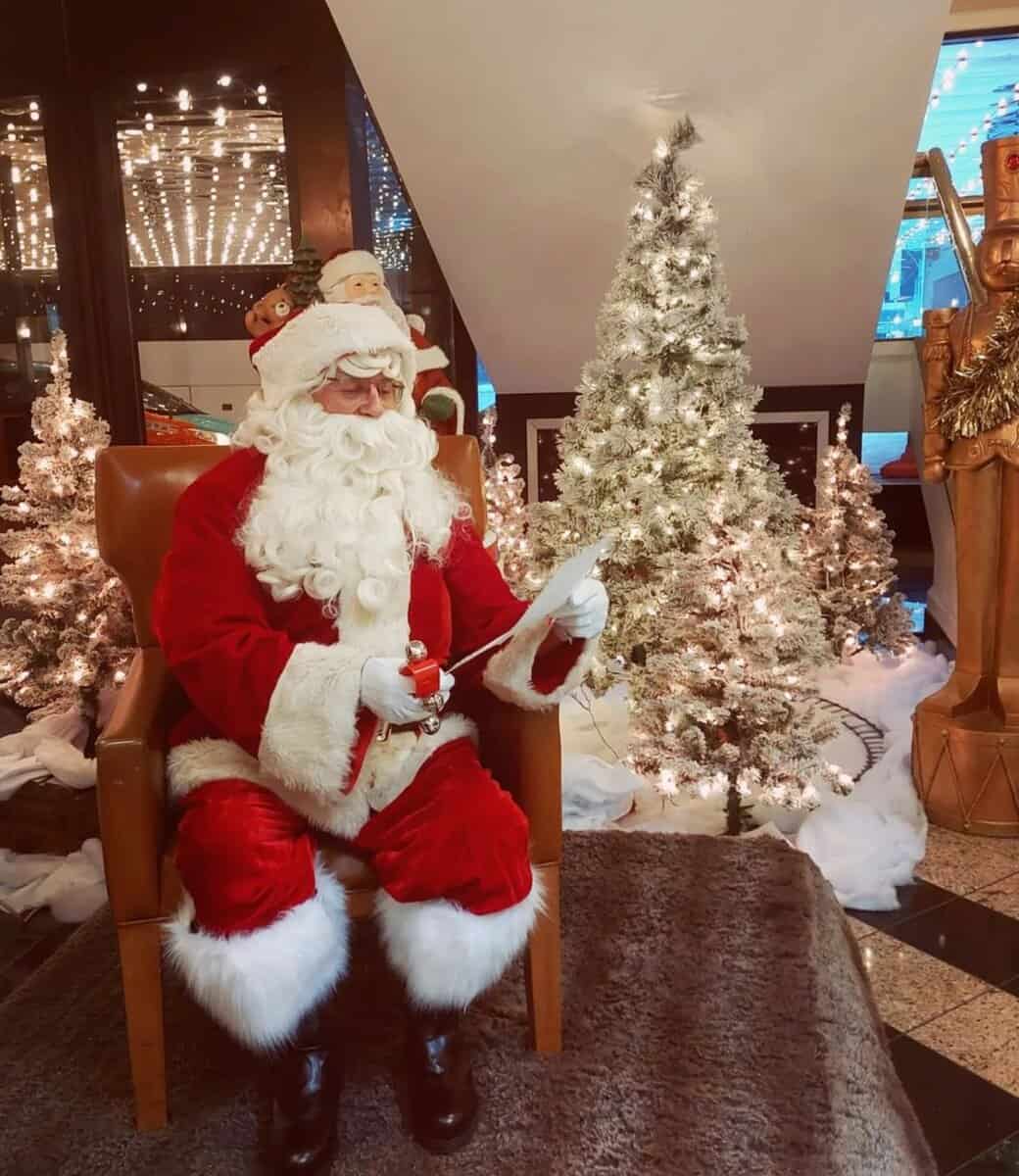 Festive Santa Claus reading holiday letter amid Christmas trees and lights in Toronto. Christmas decorations, holiday spirit, winter celebration.