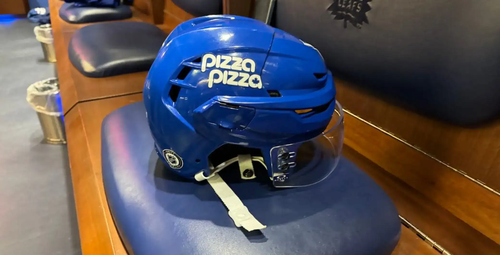 Blue Toronto Maple Leafs hockey helmet with face shield on wooden bench in sports bar setting.