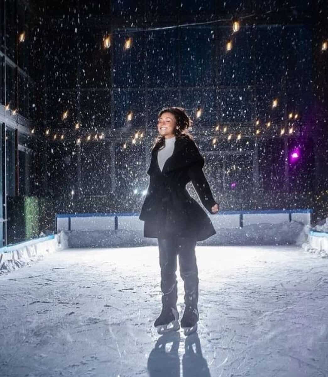 Vibrant woman ice skating at Toronto indoor rink with snow falling, Christmas lighting, festive atmosphere, winter season, Toronto entertainment scene.