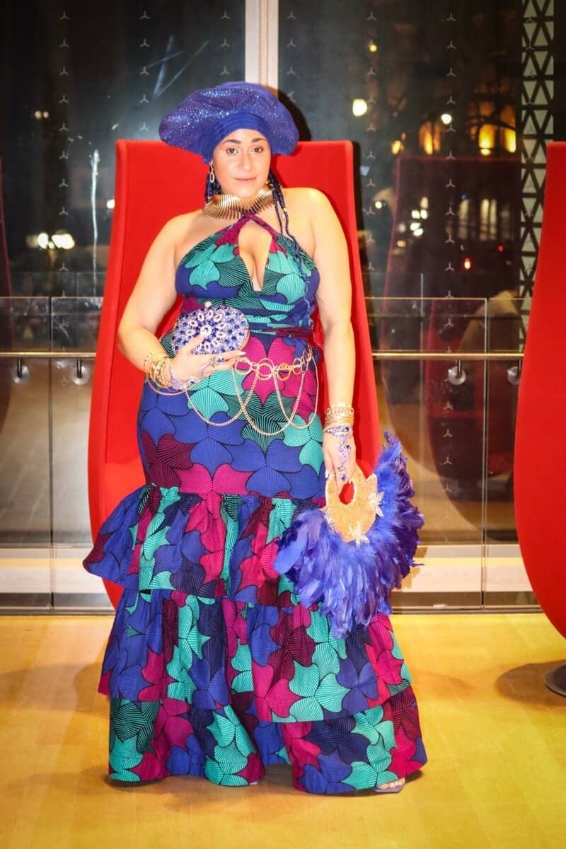 Vibrant woman in colorful patterned dress and purple feather hat at a Toronto event, showcasing fashion and cultural diversity in NOW Toronto coverage.