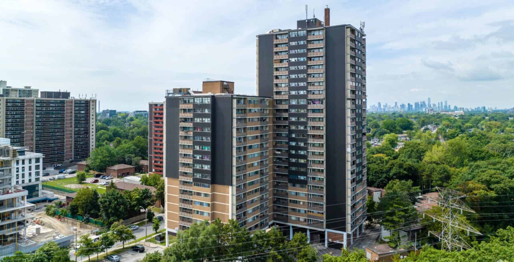 Modern high-rise residential building in Toronto with surrounding greenery and city skyline in the background.