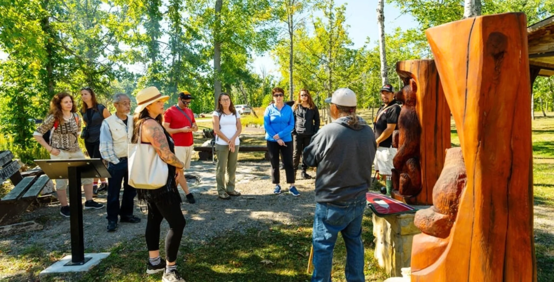 Colorful outdoor art tour in Toronto's park with diverse group, nature backdrop and wooden sculptures.
