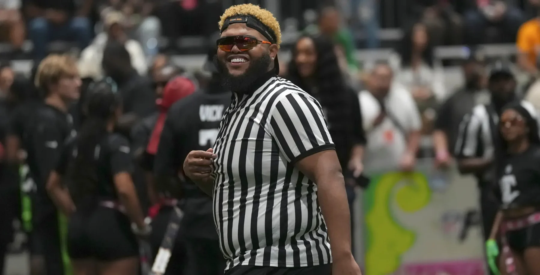Referee smiling at a football game with fans and players in the background in Toronto, Canada.