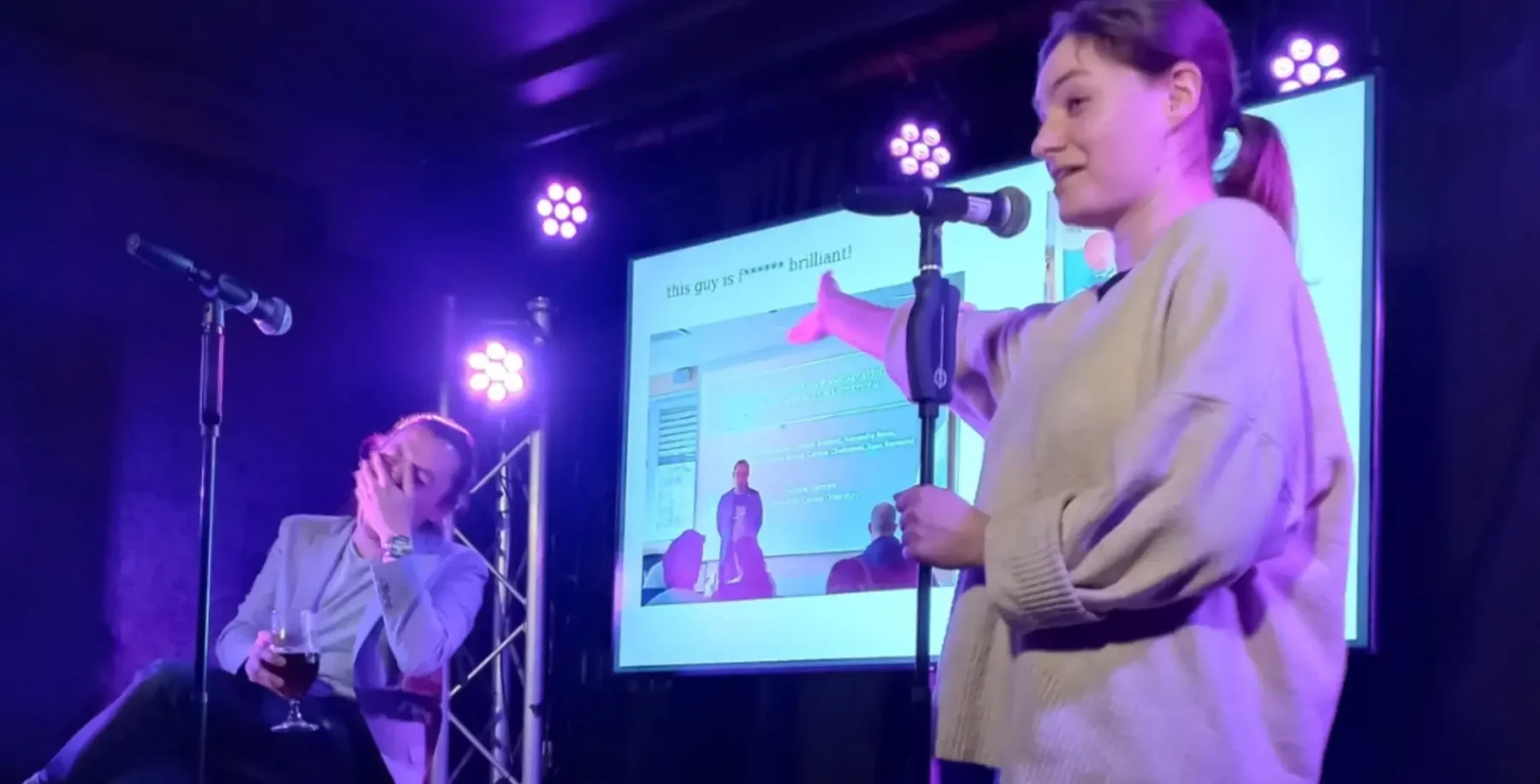 Young woman speaking into microphone at an event, on stage with presentation screen, in Toronto, Ontario.