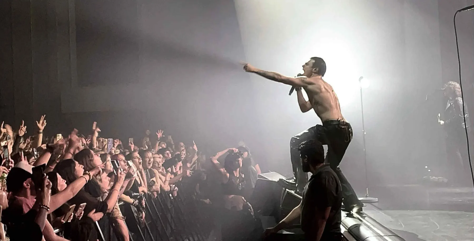 Vibrant concert scene with a shirtless male performer engaging energetic audience with fans and smartphones, spotlight illuminating stage and crowd at a live music event in Toronto.