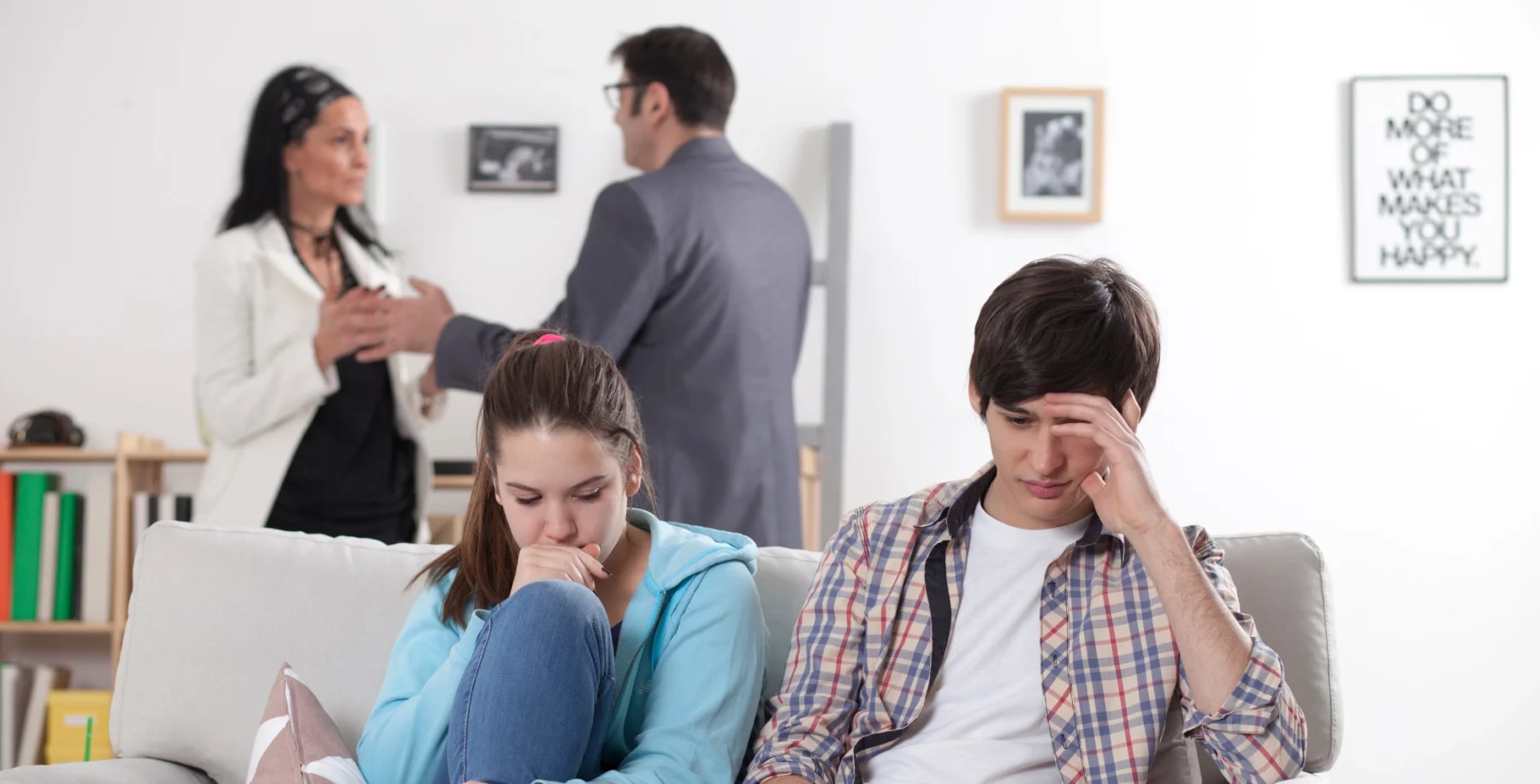 Stressed teenagers sitting on a couch with parents arguing in the background, representing family conflict and emotional distress.