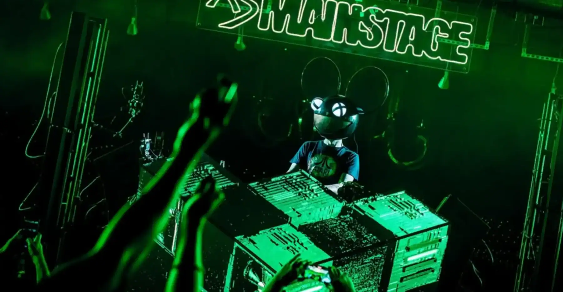 Deadmau5 wearing metallic mouse helmet at concert. Green lights fill the room.