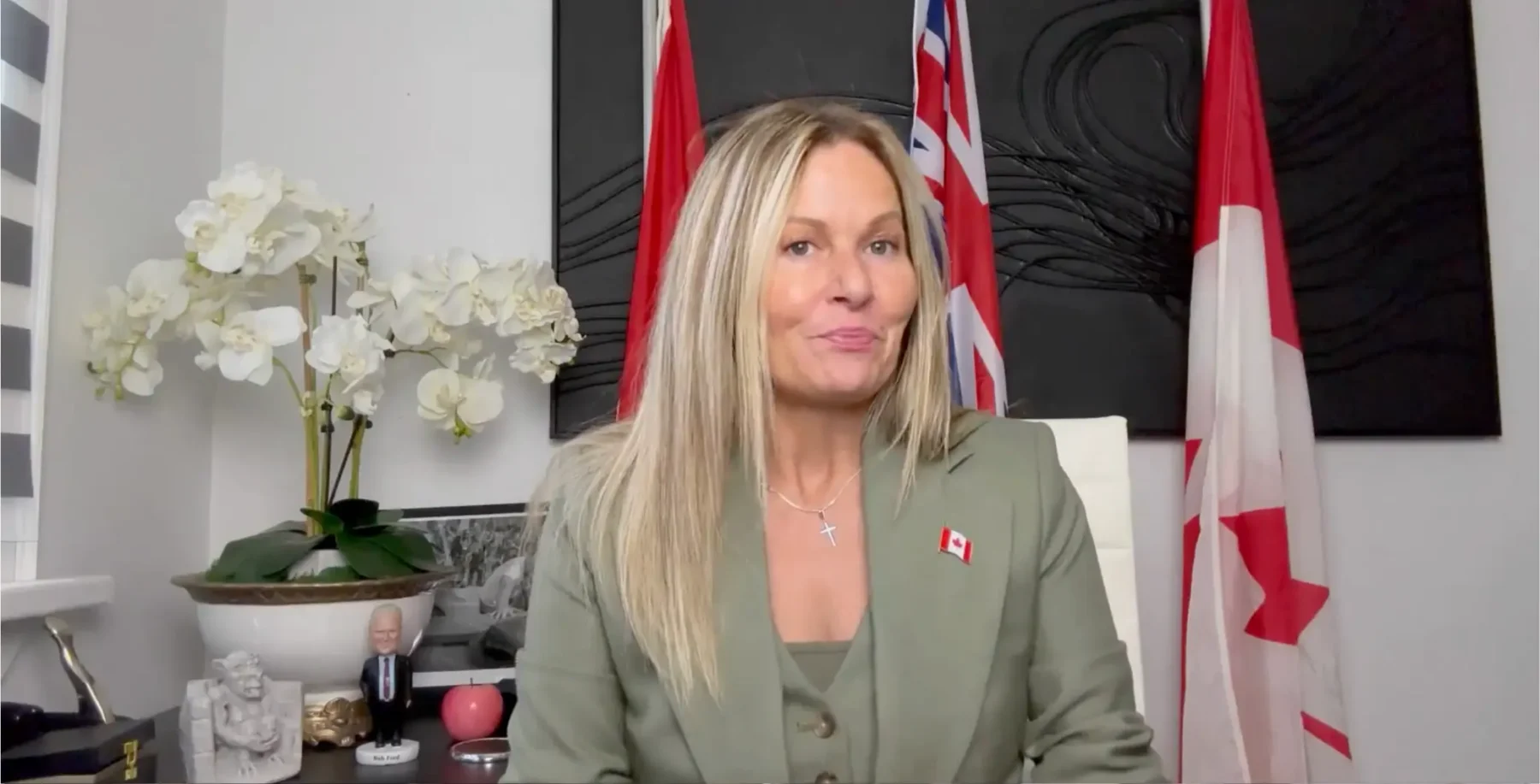 Canadian politician woman in office with Canadian flags behind her, sitting at her desk in modern office.