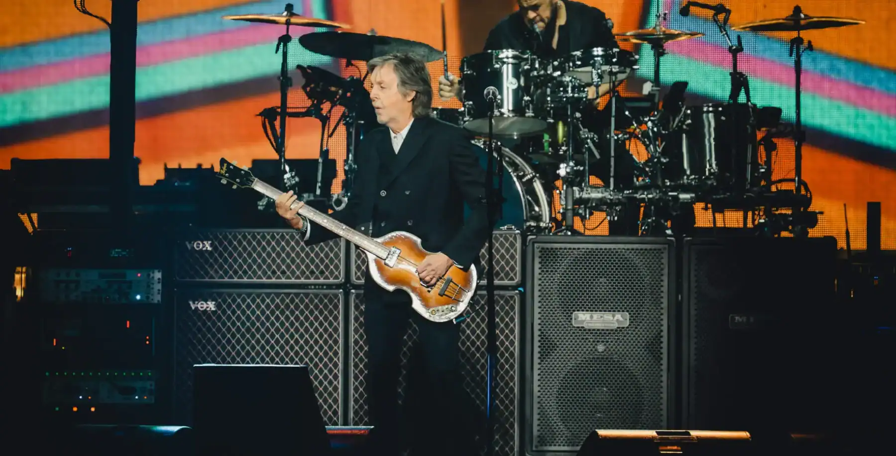 Iconic musician performing live on stage with guitar and drum set, vibrant background, Toronto concert, legendary rock artist, live music event in Toronto, music performance, Canadian music scene.