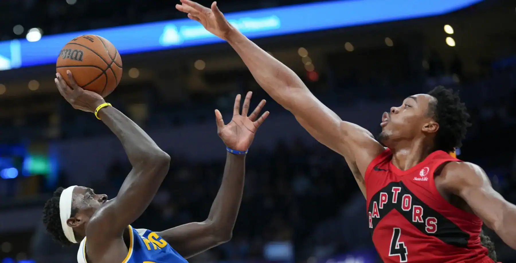 Basketball game action with player from Toronto Raptors attempting a shot against Golden State Warriors guard in high-intensity match.