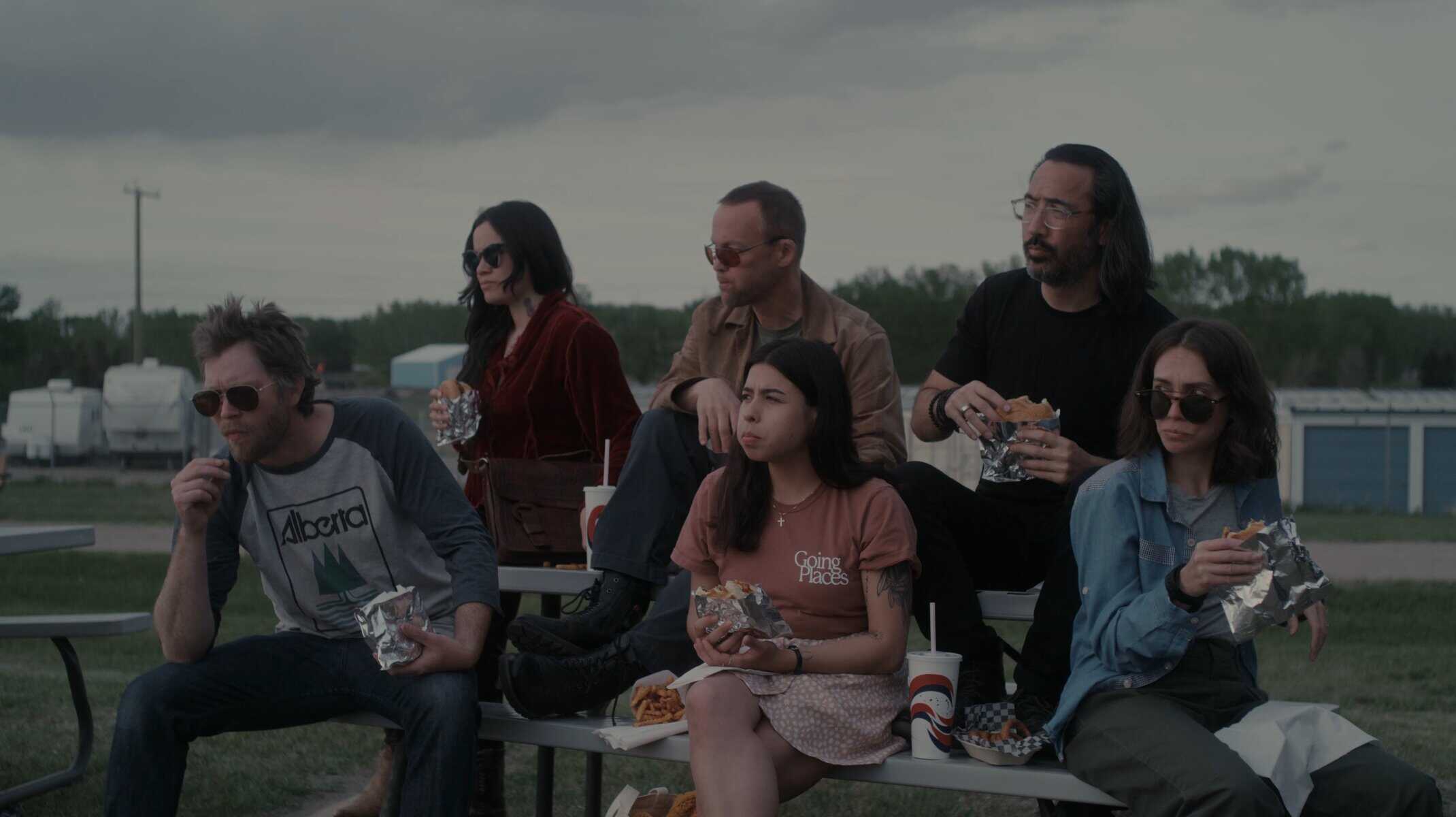 A group of people eating fast food at an outdoor setting in Canada, with a moody sky and casual atmosphere, representing Toronto lifestyle.
