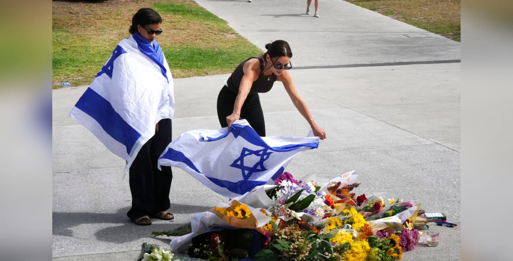 People placing flowers at a memorial with Israeli flags in Toronto, reflecting commemoration and solidarity, captured on a sunny day in an urban outdoor setting.