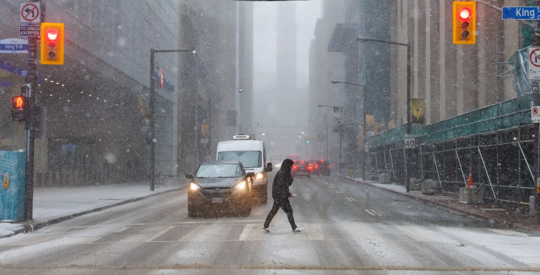 Snowy city street in Toronto during winter storm with pedestrian crossing the road.