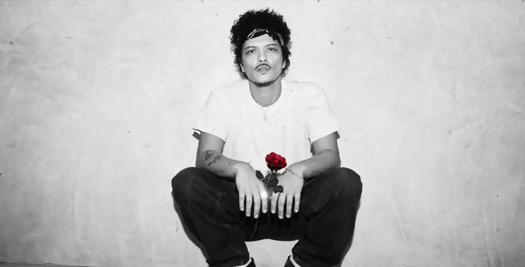 Young man with curly hair holding a red rose, black and white image, urban background, expressive style, contemporary fashion, Toronto culture, street art vibe.