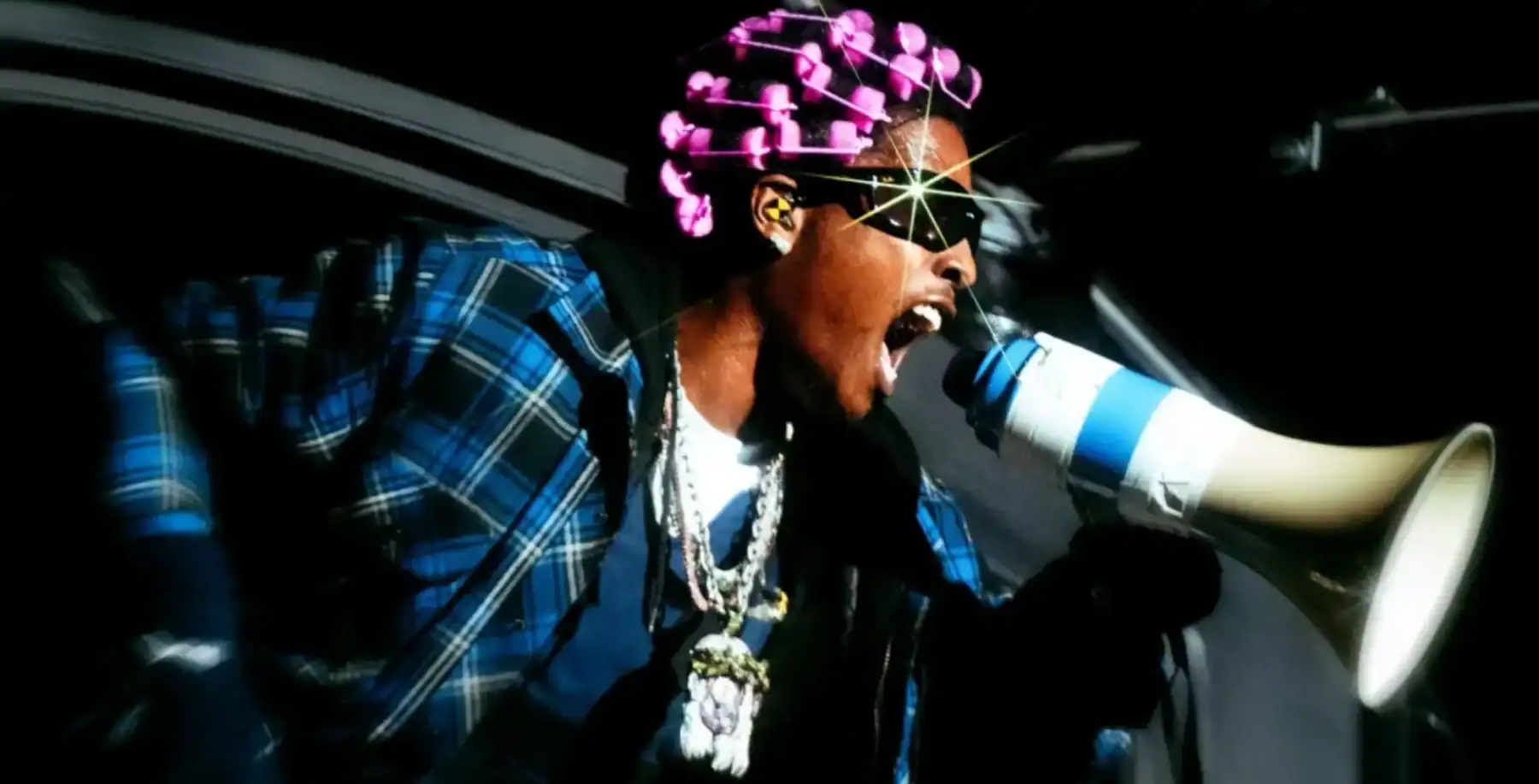 Bold, energetic performer with pink hair and sunglasses using a megaphone in a dynamic Toronto street scene.
