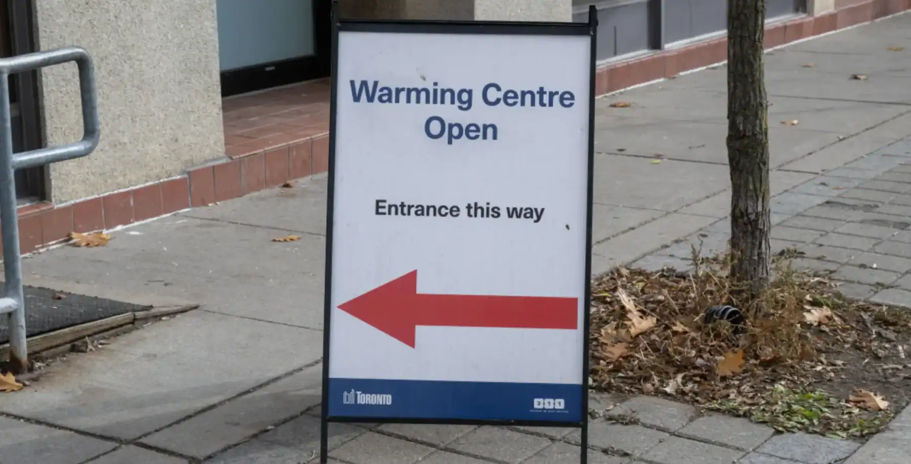 Warming Centre Open sign on a city sidewalk in Toronto, indicating the entrance to a homeless warming shelter during cold weather.