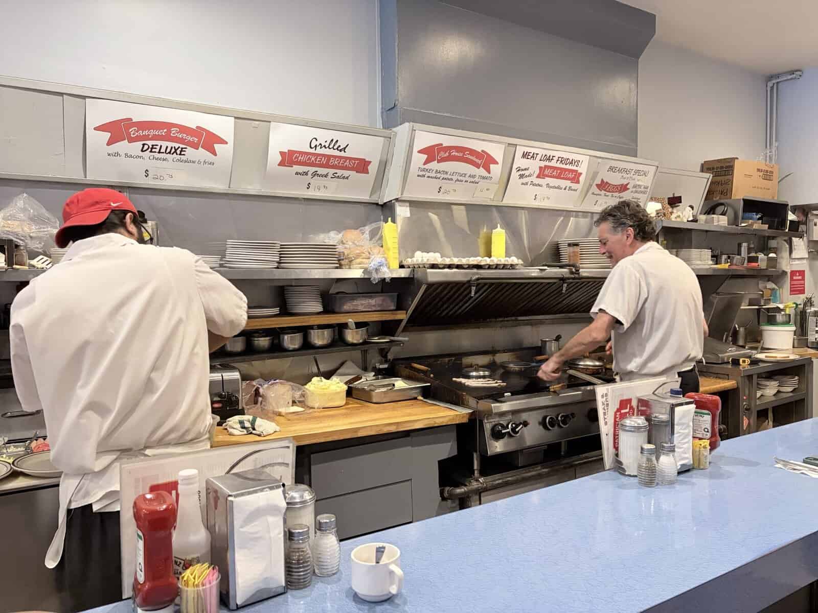 Grilled chicken being prepared in a busy restaurant kitchen with chefs working at the stove and cooking station.