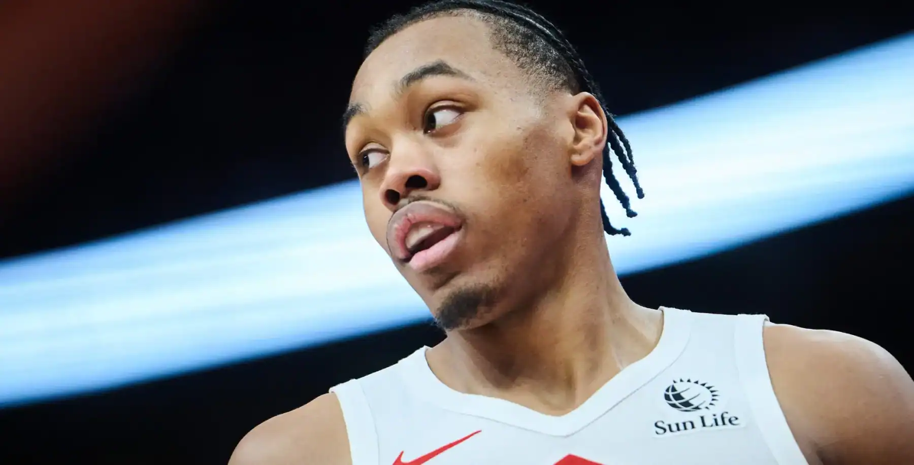 A young male athlete with braided hair, wearing a white sports jersey with Sun Life logo, looking to the side during a game or practice, in an indoor sports facility.