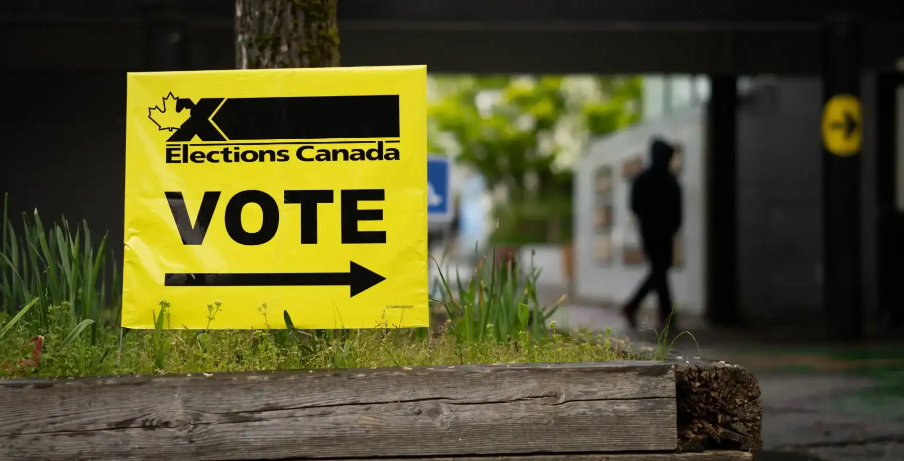 A bright yellow "VOTE" sign with an arrow pointing towards a polling station during Canadian elections, encouraging voter participation and civic engagement.