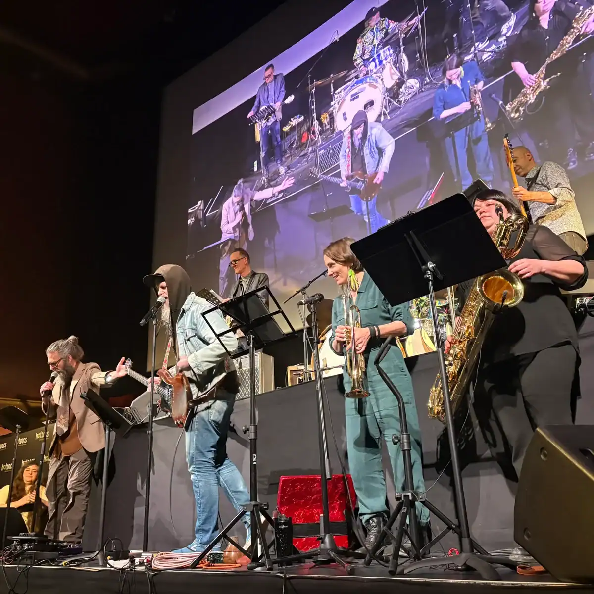 Live performance at the Nash The Slash documentary event showcasing Toronto's iconic music pioneer with musicians on stage and a large screen in the background.