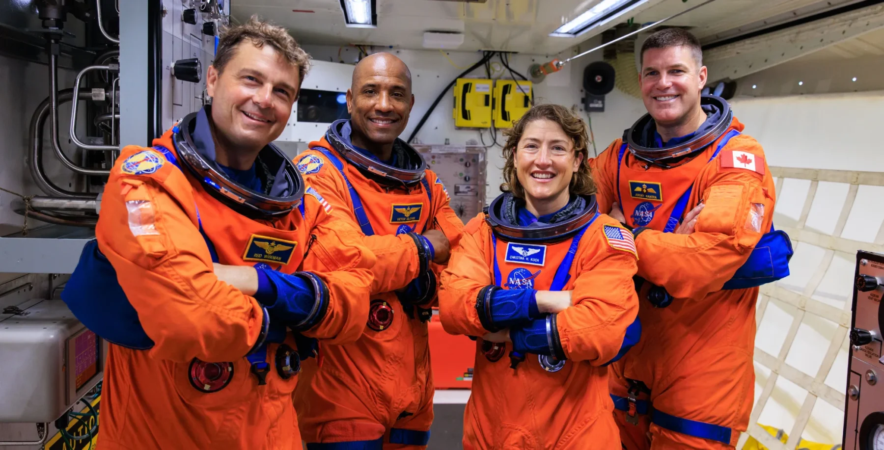 An image of four Canadian astronauts in orange space suits smiling inside a spacecraft, preparing for NASA’s first moon trip in over 50 years, highlighting Canada's role in space exploration.