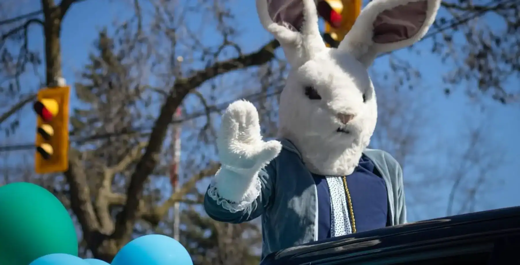 Festive Easter Bunny mascot waving during Toronto parade with balloons and clear blue sky, celebrating the Easter long weekend in Toronto.