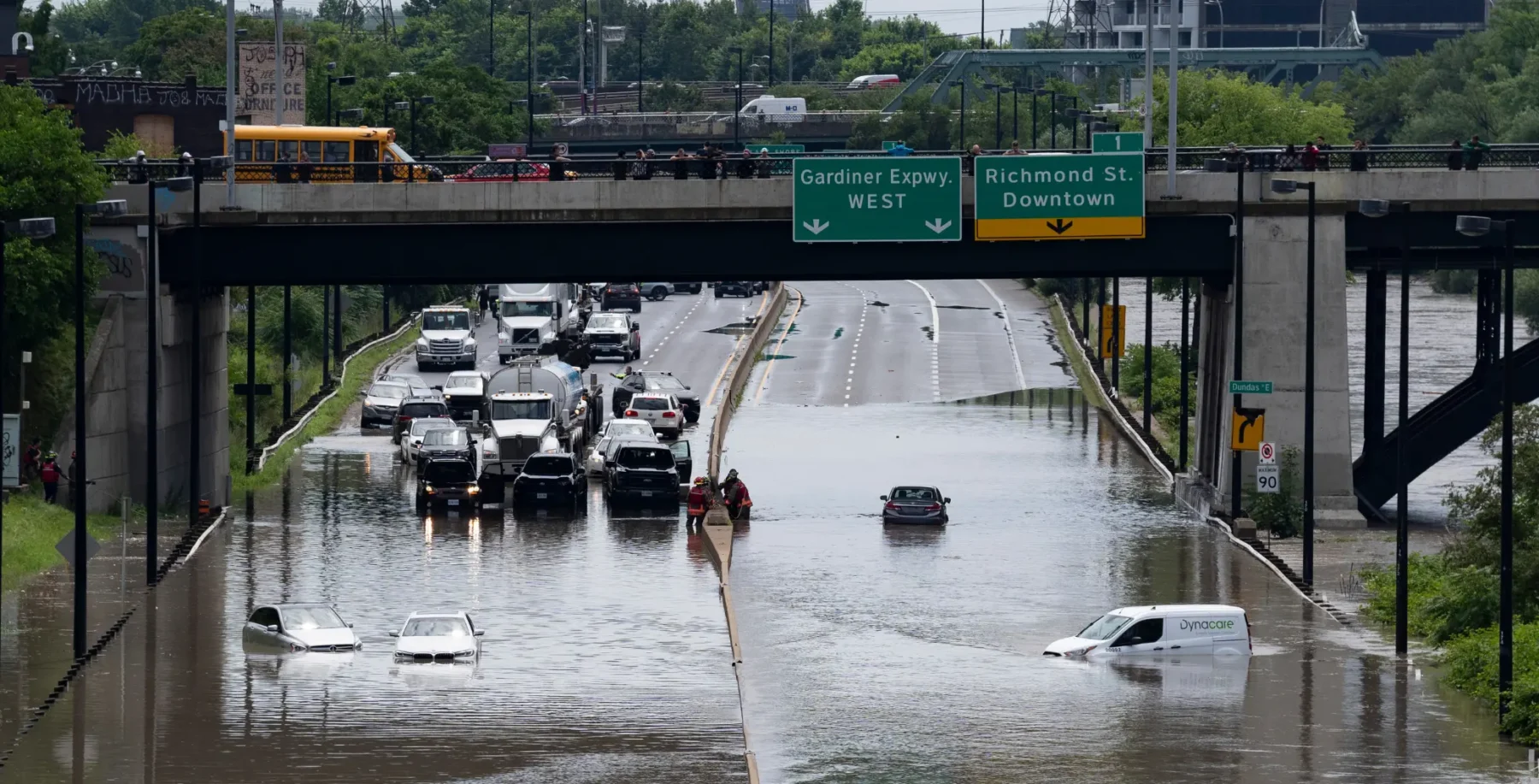 City street submerged in floodwaters with vehicles and pedestrians navigating through the heavy rain, highlighting concerns about flooding preparedness in Toronto.