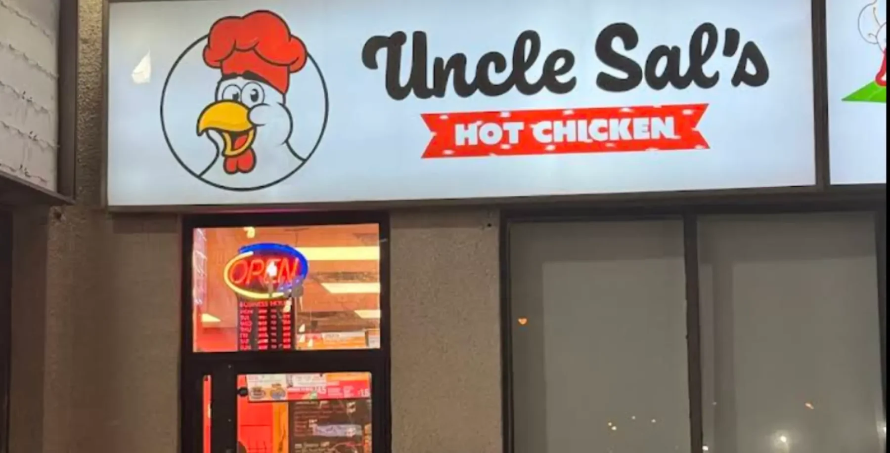 Exterior view of Uncle Sal's Hot Chicken restaurant sign in Toronto, featuring a cartoon chicken mascot and bright "Open" sign, highlighting local dining options.