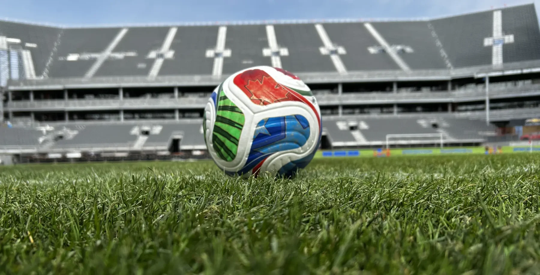 Soccer ball on the field at a stadium, highlighting FIFA's last-minute ticket release for the World Cup, with empty stands in the background.