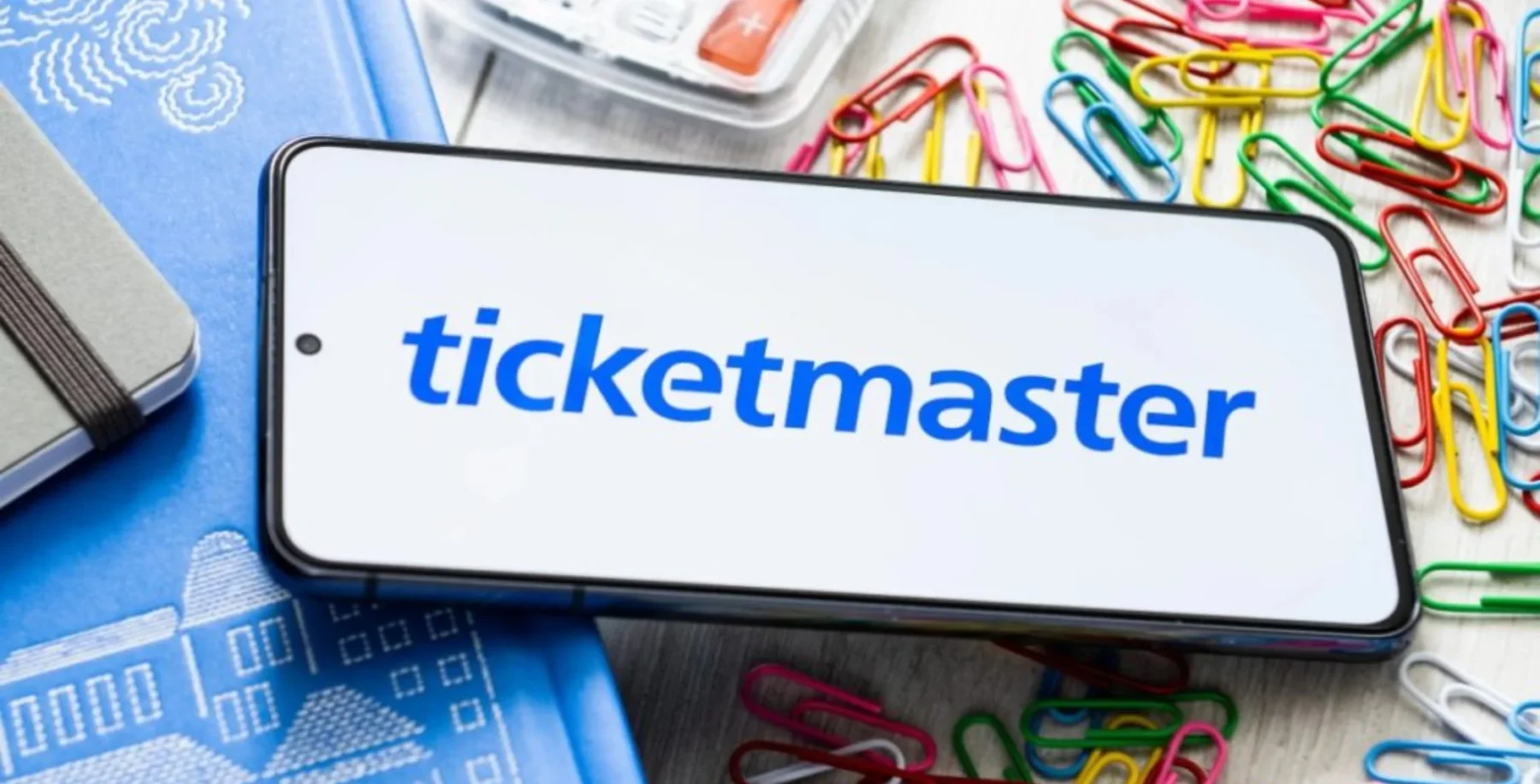 Ticketmaster mobile app displayed on smartphone screen, surrounded by office supplies and colorful paper clips, representing event tickets and entertainment in Toronto.