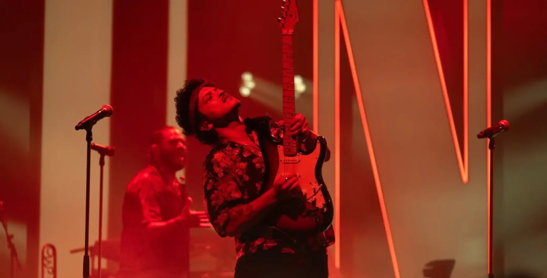 A musician passionately playing an electric guitar on stage during a live performance at a NOW Toronto event, illuminated by vibrant red lighting, capturing the energy of Toronto's music scene.
