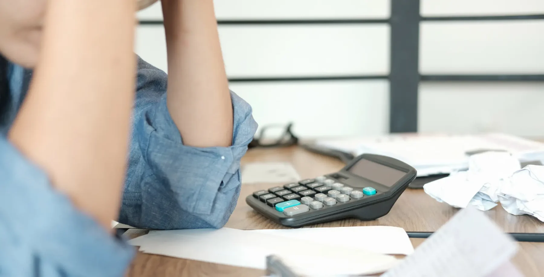 A person working at a cluttered desk with papers and a calculator, possibly doing financial or administrative tasks, in an office setting.
