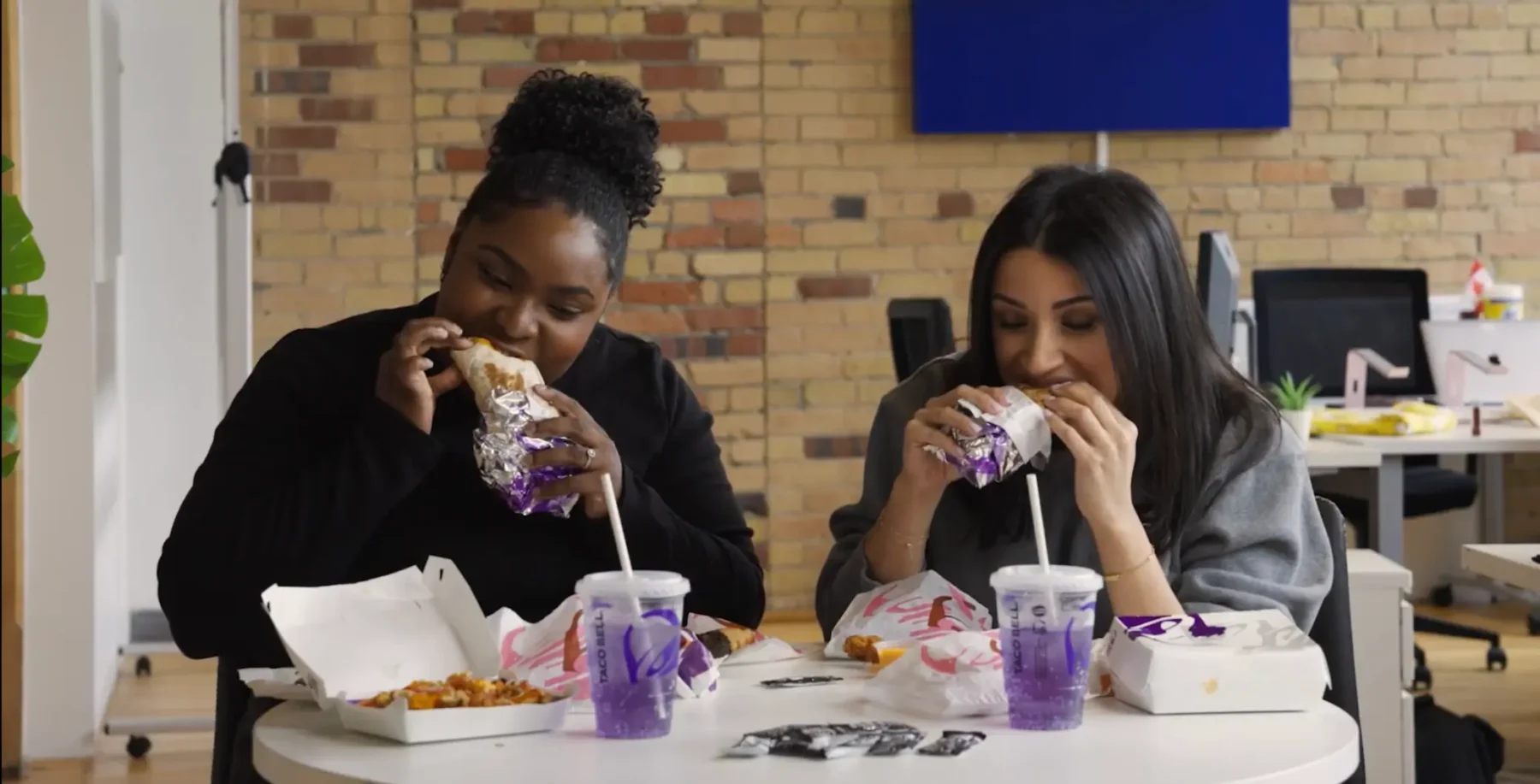 Two women enjoying Taco Bell Diablo Buffalo menu items in a casual dining setting, showcasing the spicy new lineup with drinks and food on a modern table.