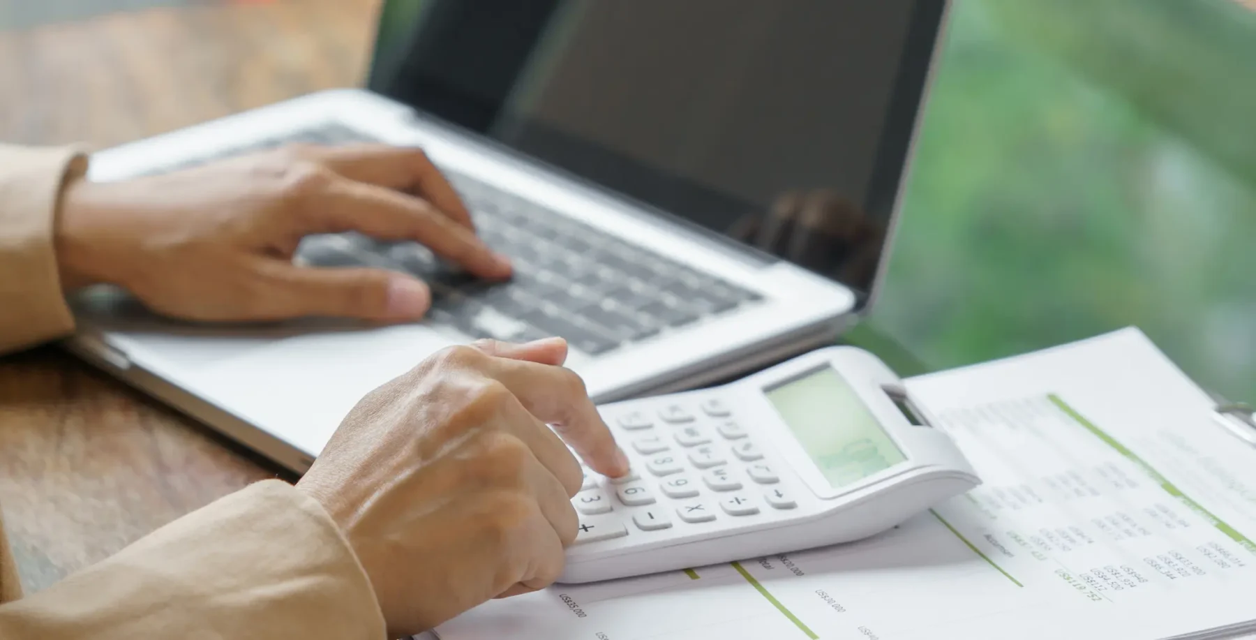 Person using a calculator and laptop on a desk with documents, representing financial analysis or accounting work in Toronto.