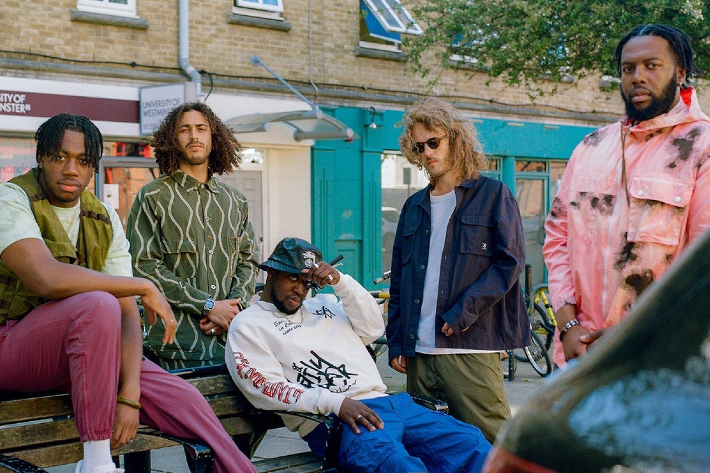 Ezra Collective band members posing outdoors in casual attire on a city street, promoting their Here Because of Hope Tour, with a vibrant urban background.