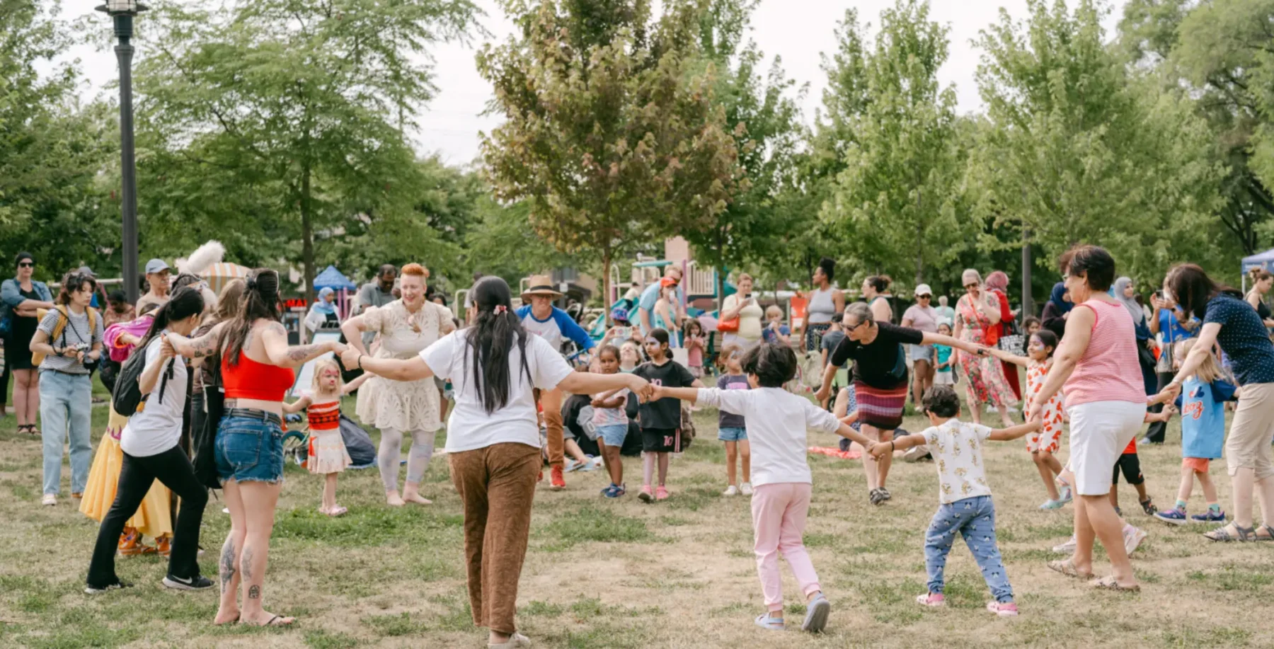 Community outdoor festival in Etobicoke with families dancing and children playing in a park setting.