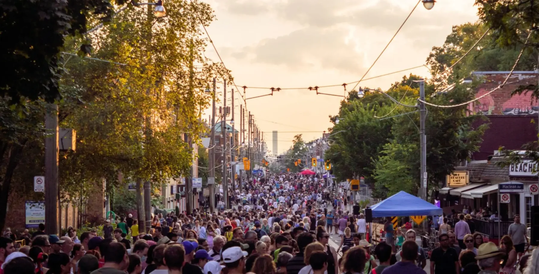Crowd of people on Queen Street East during a lively outdoor music festival in Toronto with trees and streetcars in the background.
