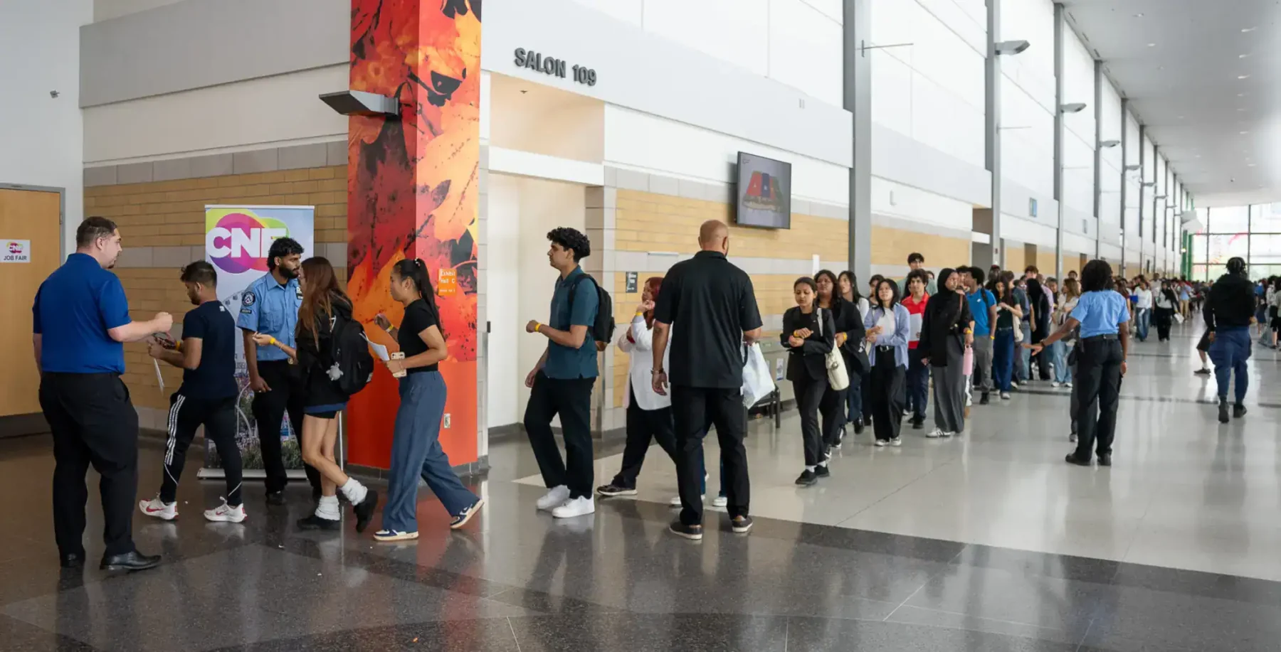 People waiting in line at the CNE job fair in Toronto, with diverse individuals and a modern convention centre interior.
