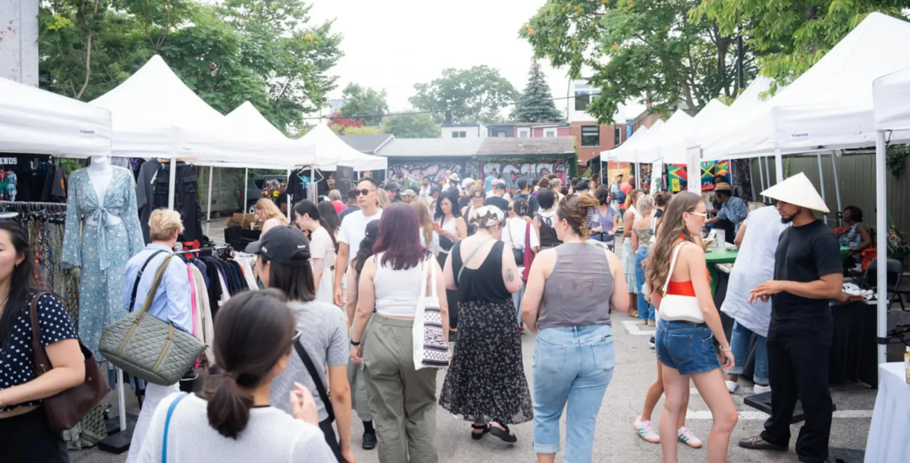 Crowd of people enjoying OssFest street festival on Ossington in Toronto with vendor tents and green trees in the background.