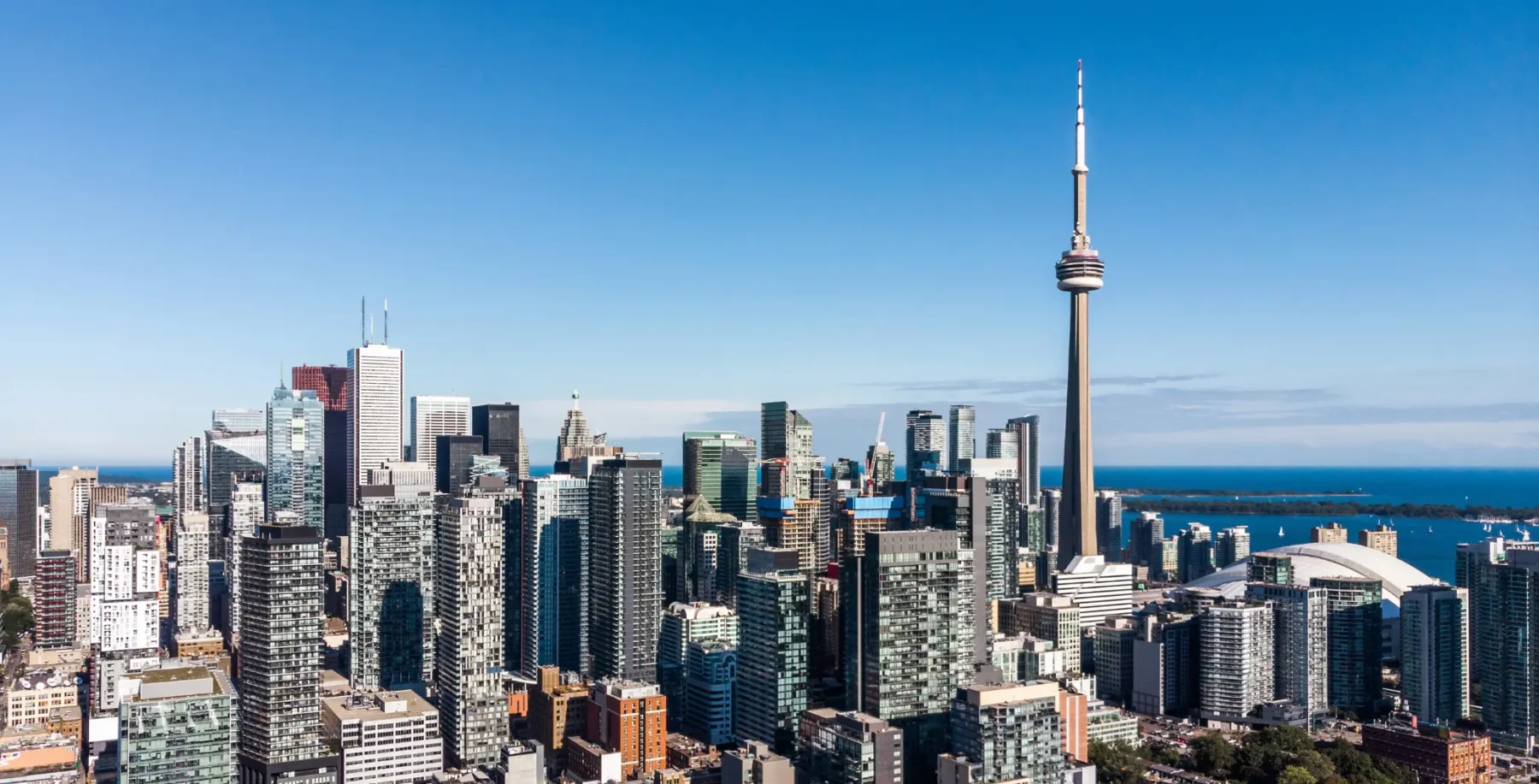 Toronto skyline with CN Tower under clear blue sky, showcasing modern skyscrapers and cityscape.