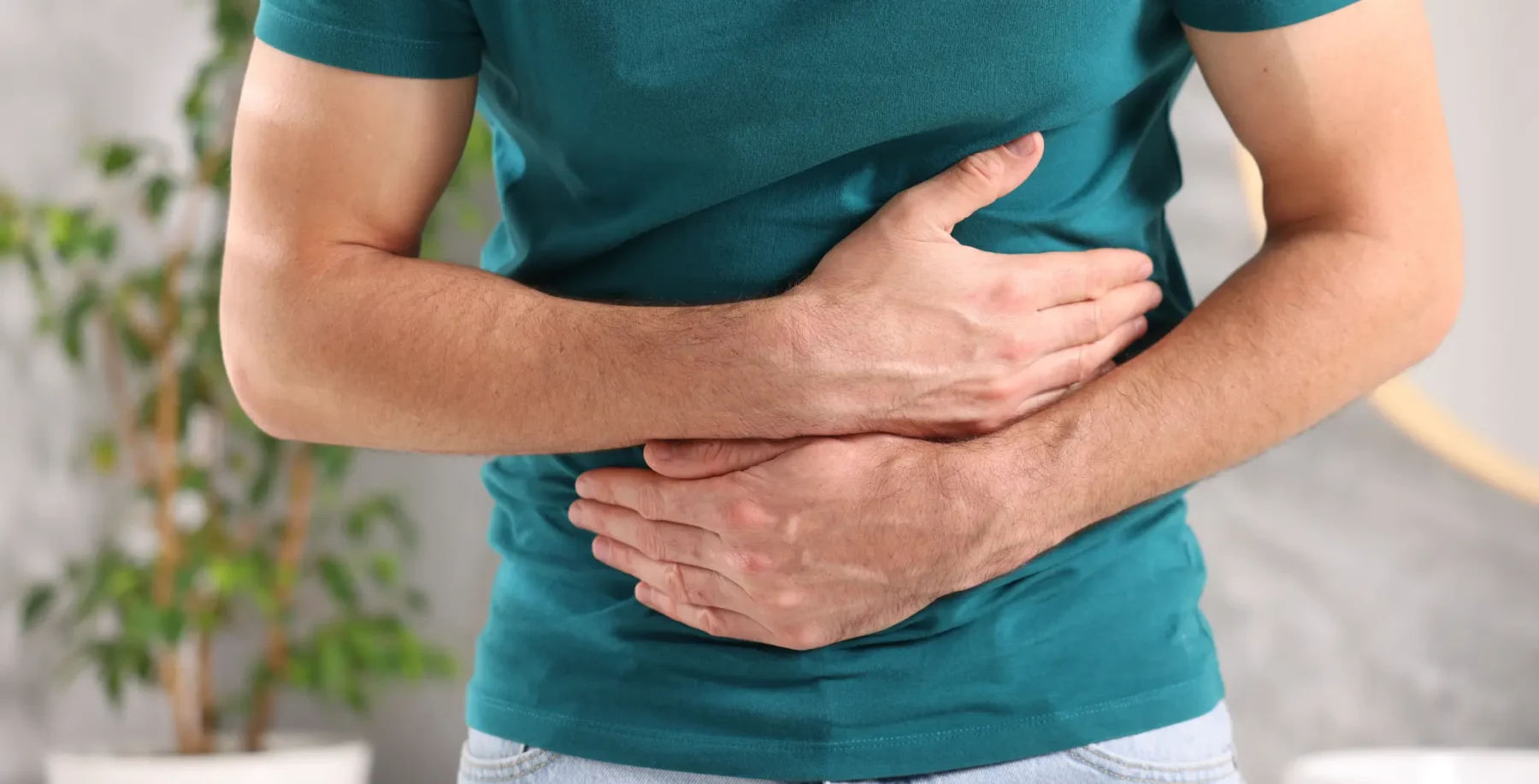 Person holding stomach, indicating abdominal pain or discomfort, in a well-lit indoor setting.